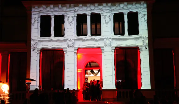 Clădire istorică albă, cu intrarea accentuată în lumină roșie